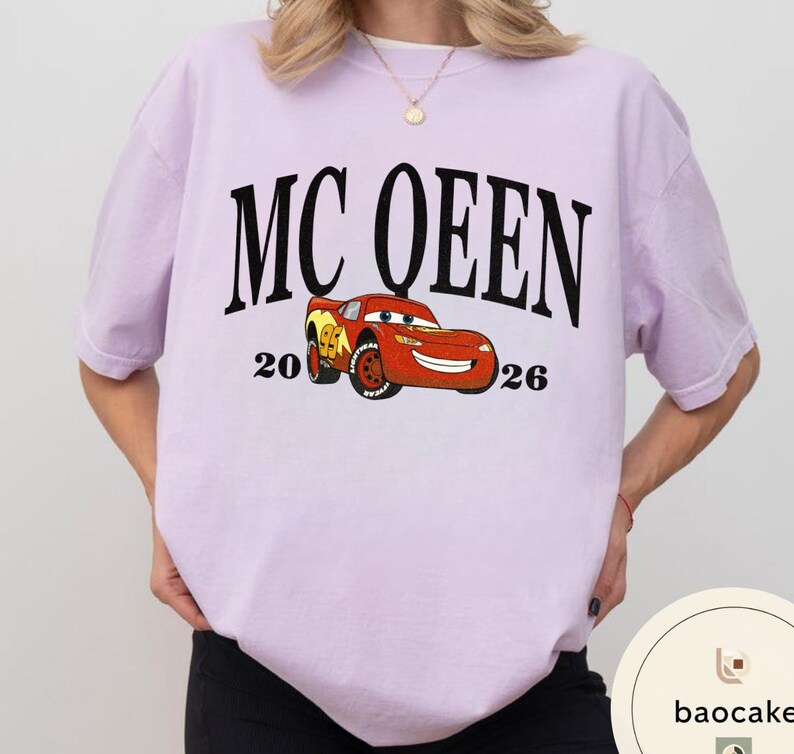 May include: A light purple t-shirt featuring the text "MC QUEEN" in large black letters above a cartoon image of a red race car. The numbers "20" and "26" flank the car. The shirt is a casual style.