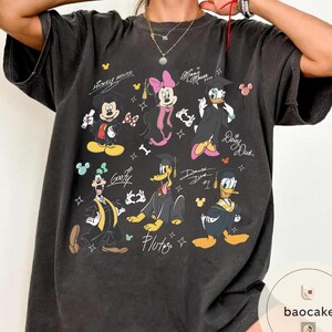 May include: Dark gray t-shirt featuring cartoon characters Mickey Mouse, Minnie Mouse, Donald Duck, Daisy Duck, Goofy, and Pluto in graduation attire. The shirt includes the text "Mickey Mouse", "Minnie Mouse", "Daisy Duck", and "Pluto".
