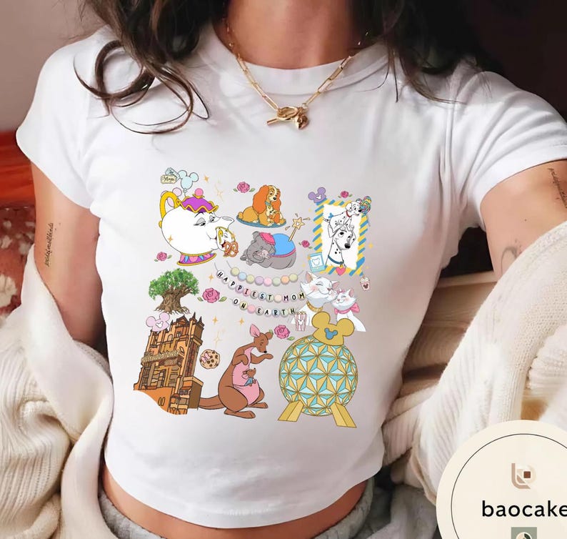 May include: White t-shirt with a colorful graphic featuring cartoon characters and the text "Happiest Mom on Earth." The design includes a teapot, dog, elephant, and kangaroo. The shirt is made of a soft material.