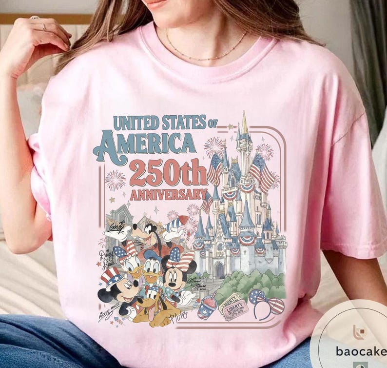 May include: Light pink t-shirt featuring a graphic celebrating the 250th anniversary of the United States of America. The design includes a castle, fireworks, and cartoon characters in patriotic attire.