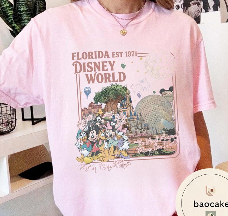 May include: A light pink short-sleeve t-shirt featuring a graphic print of Disney World landmarks and characters. The text reads FLORIDA EST 1971, DISNEY WORLD, and The Most Magical Place On Earth, accompanied by illustrations of Mickey, Minnie, and friends.