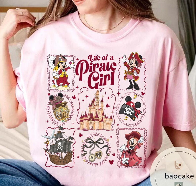May include: Pink t-shirt featuring a design with the text "Life of a Pirate Girl" and illustrations of a pirate-themed Minnie Mouse. The design includes a pirate ship, treasure chest, and a castle.