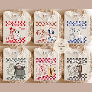 May include: Cream-colored t-shirts featuring various characters from 101 Dalmatians. Designs include Pongo, Patch, Perdita, Horace, Cruella, and Jasper, each with a name and the text "Est. 1961" above a checkered pattern. The shirts are folded on a woven surface.
