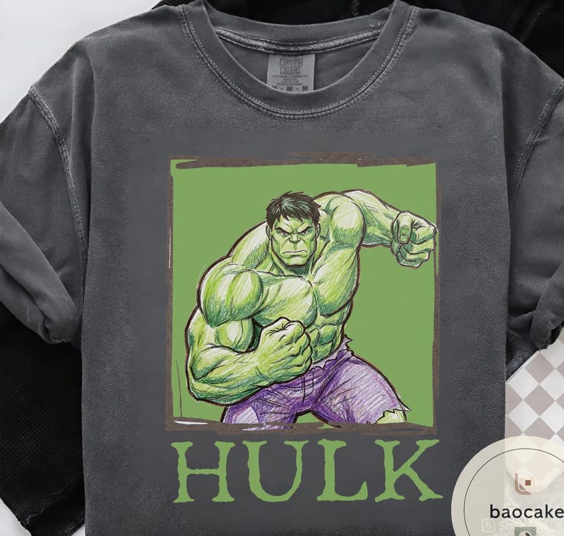 May include: Dark gray t-shirt featuring a green illustration of the Hulk in a fighting pose, set against a green background. The word "HULK" is printed in green below the image. The shirt has a crew neck and short sleeves.