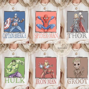 May include: Cream-colored t-shirts featuring superhero graphics. Designs include Captain America, Spider-Man, Thor, Hulk, Iron Man, and Groot, each within a colored frame and labeled with their name. The shirts have a round neckline.