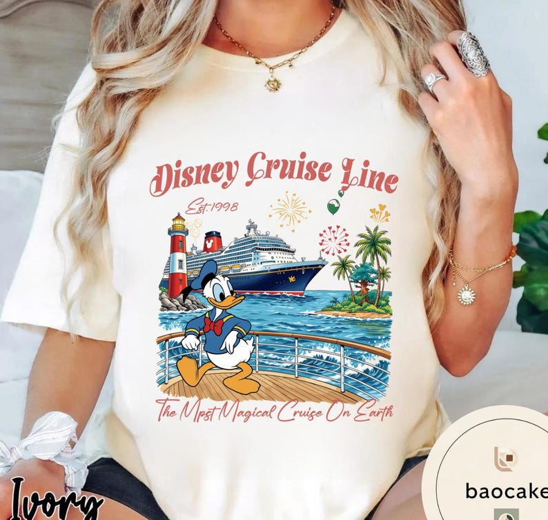 K&ouml;nnte beinhalten: Elfenbeinfarbenes T-Shirt mit einer Grafik von Donald Duck auf einem Kreuzfahrtschiff. Das Design umfasst einen Leuchtturm, Palmen und den Text "Disney Cruise Line" und "The Most Magical Cruise On Earth."