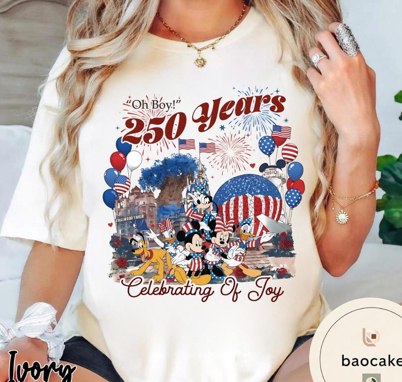 Puede incluir: Camiseta de color marfil con un dise&ntilde;o patri&oacute;tico con Mickey Mouse, Donald Duck y Pluto. La camiseta incluye el texto "Oh Boy! 250 Years Celebrating Of Joy" con fuegos artificiales, globos y banderas americanas.