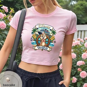 May include: Pink crop top featuring a Disney cruise ship graphic with Chip and Dale at the helm. The design includes palm trees, waves, and the word "Destiny". The shirt has short sleeves.