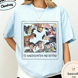 May include: Pale blue t-shirt with a graphic of Toy Story characters wearing graduation caps. The image is framed with the text "TO KINDERGARTEN AND BEYOND". The shirt has short sleeves and a crew neck.
