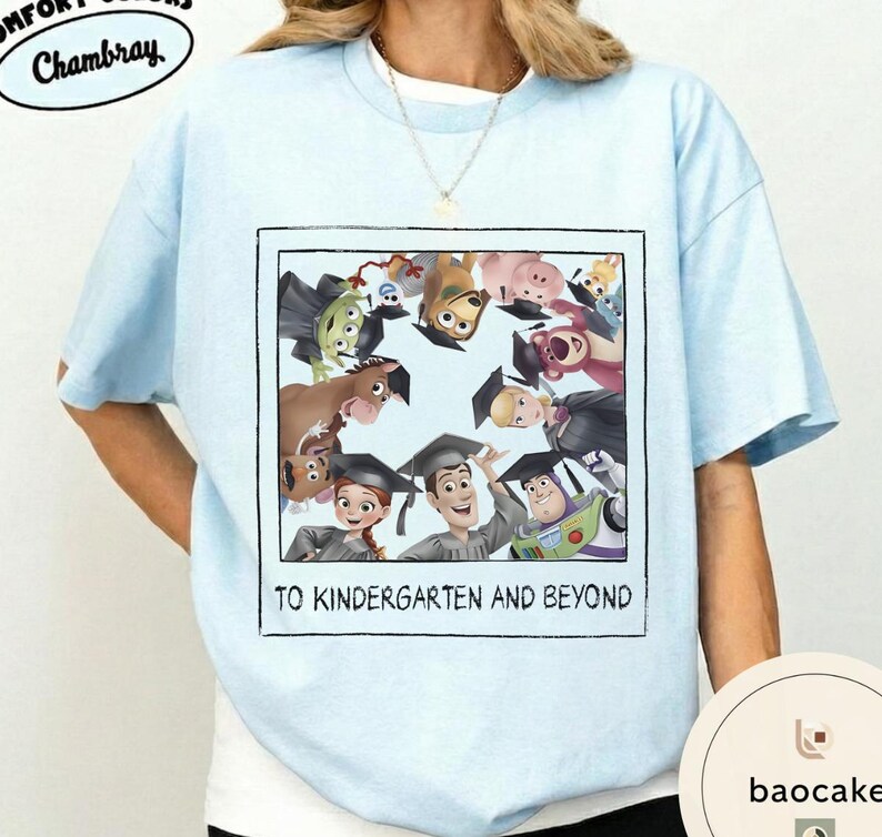 May include: Pale blue t-shirt with a graphic of Toy Story characters wearing graduation caps. The image is framed with the text "TO KINDERGARTEN AND BEYOND". The shirt has short sleeves and a crew neck.