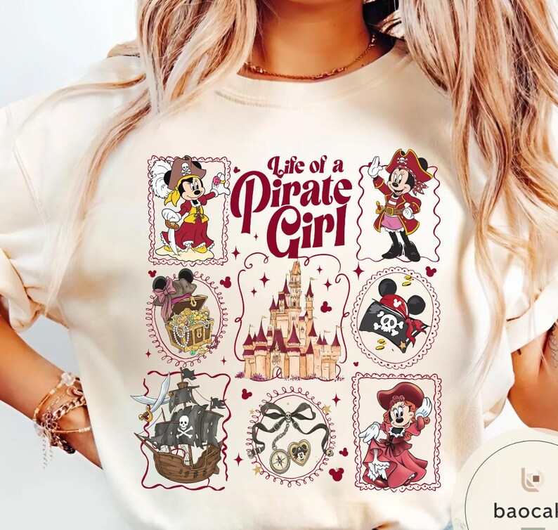 May include: Cream-colored t-shirt featuring a "Life of a Pirate Girl" design. The design includes illustrations of Minnie Mouse in pirate attire, a treasure chest, a pirate ship, a castle, and other pirate-themed elements.