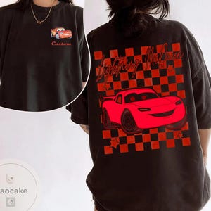 May include: Black t-shirt featuring a red cartoon car design. The front of the shirt has a small car graphic and the word "Custom". The back of the shirt has a larger car graphic with the words "Lightning McQueen" and a checkered background.