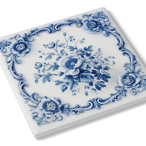 May include: Square white ceramic tile with a blue floral design. The tile features a central bouquet of blue flowers surrounded by a decorative blue border with floral accents. The tile is a square shape.