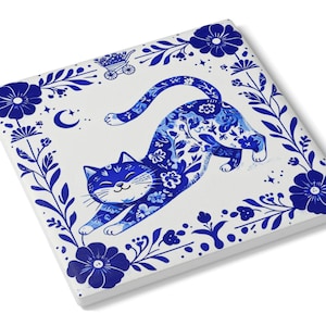 May include: Square ceramic tile featuring a blue cat stretching, with floral patterns and a decorative border. The cat and border are in a deep blue color against a white background. The design includes a crescent moon and a small cart.