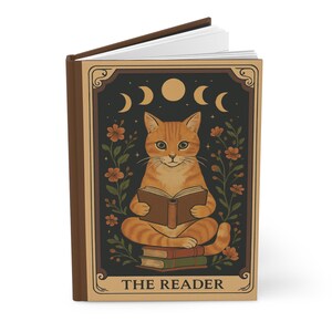 May include: A brown journal with a cat illustration. The cat is orange and reading a book, with a stack of books at its feet. The journal cover has a dark background with moons, flowers, and the text "THE READER".