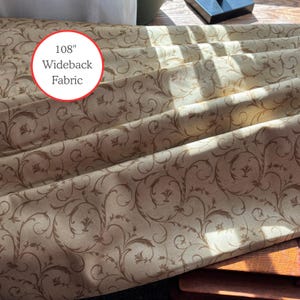 May include: Beige wideback fabric featuring a repeating brown floral scroll pattern. The fabric is 274 cm wide. The fabric is folded, showing the detailed design and texture. The text "108" Wideback Fabric" is in a red circle.