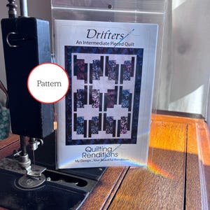 May include: A sewing machine with a pattern titled "Drifters" for an intermediate pieced quilt. The pattern features a geometric design with purple, blue, and white blocks. The pattern is from Quilting Renditions.