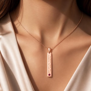 Op de afbeelding: Rosegouden hangerketting met een rechthoekige bedel. De bedel heeft de gegraveerde tekst "you are my sunshine, my only sunshine" en een kleine rode edelsteen. De ketting wordt door een persoon gedragen.