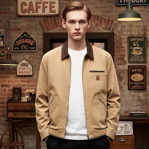 May include: A tan jacket with a brown corduroy collar and a white t-shirt underneath. The jacket has a zipper closure, a chest pocket, and two side pockets. The background is a brick wall with vintage signs.