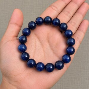 May include: A circular bracelet composed of smooth, polished, deep blue spherical beads. The beads are uniform in size and strung together in a continuous loop, displaying a consistent dark navy color with subtle variations in light reflection.