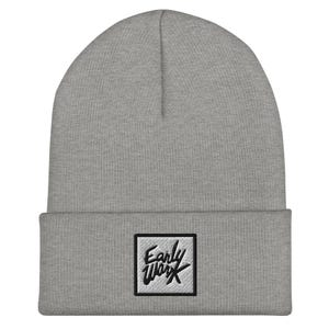May include: A light gray beanie hat with a folded brim. The hat features a square patch with the text "Early Work" embroidered in black. The beanie is made of a soft, knitted material.