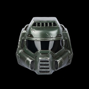 May include: A metallic green helmet with a dark visor, reminiscent of a futuristic space suit. The helmet has a detailed design with vents and ridges, suggesting a sci-fi or gaming theme. The background is solid black.