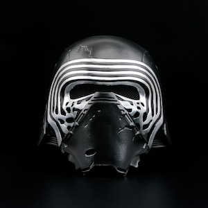 May include: A black and silver Kylo Ren helmet, a Star Wars character. The helmet features a unique design with horizontal silver stripes and detailed patterns around the face. The background is black.