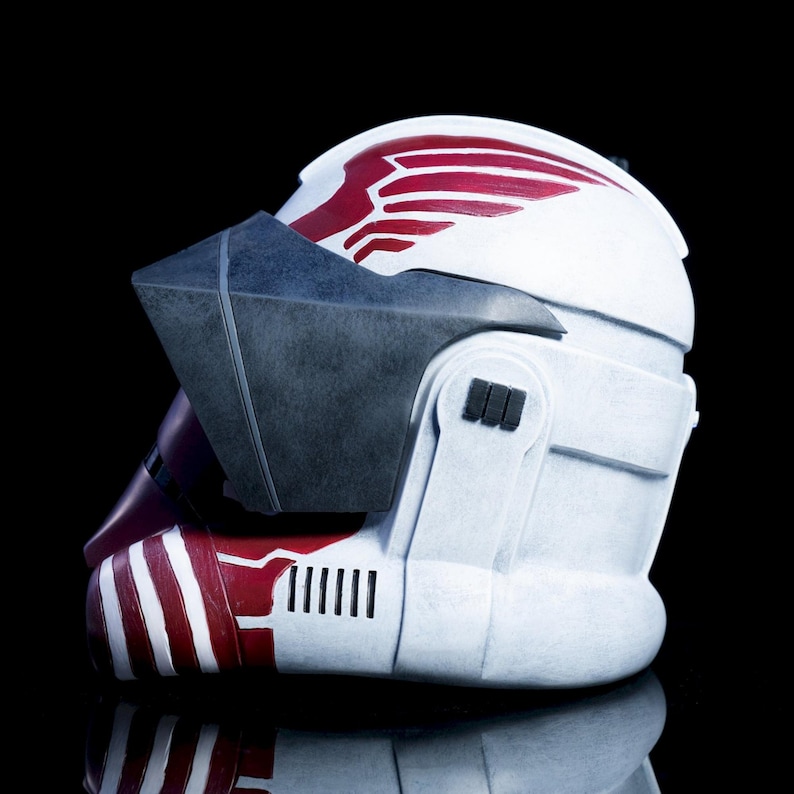 May include: A white and red helmet with a dark visor. The helmet has red markings on the top and sides, with a series of vertical black lines. The visor is a dark gray color. The helmet is set against a black background.