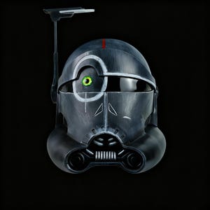 Può includere: Un casco grigio scuro con un occhio verde e una striscia rossa. Il casco ha una visiera e un dispositivo di comunicazione. Il casco è una replica di un personaggio di un film di fantascienza.