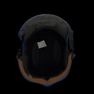 May include: A blue motorcycle helmet with a black interior and a brown trim. The helmet has a black strap and a label inside. The image is taken from a top-down perspective against a black background.