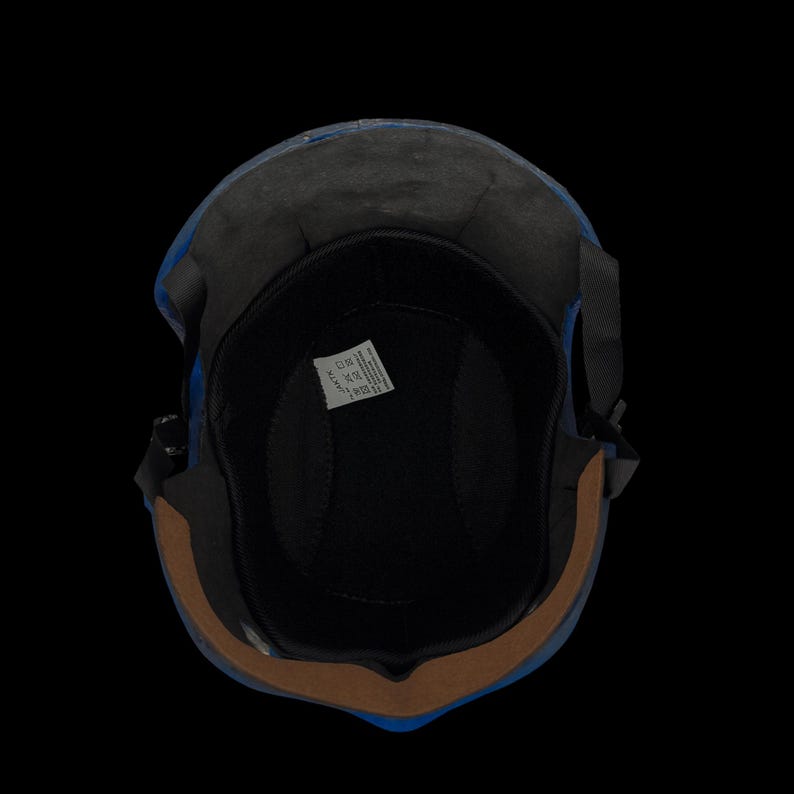 May include: A blue motorcycle helmet with a black interior and a brown trim. The helmet has a black strap and a label inside. The image is taken from a top-down perspective against a black background.