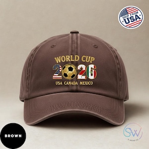 May include: A brown baseball cap featuring the text "WORLD CUP 2026" and a soccer ball graphic. The numbers 2026 incorporate the flags of USA, Canada, and Mexico. The cap also displays "USA CANADA MEXICO".