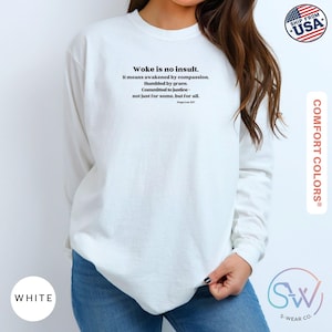 May include: White long-sleeve sweatshirt with the text "Woke is no insult" and a quote about compassion and justice. The sweatshirt is from Comfort Colors and has a "Ship from USA" graphic.