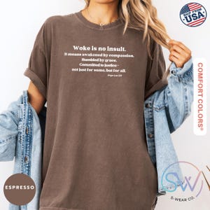 May include: Espresso-colored t-shirt with the text "Woke is no insult." in white. The quote continues with "It means awakened by compassion. Humbled by grace. Committed to justice - not just for some, but for all." The shirt is from Comfort Colors.