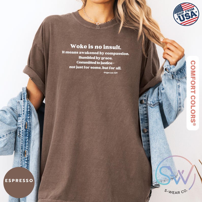 May include: Espresso-colored t-shirt with the text "Woke is no insult." in white. The quote continues with "It means awakened by compassion. Humbled by grace. Committed to justice - not just for some, but for all." The shirt is from Comfort Colors.