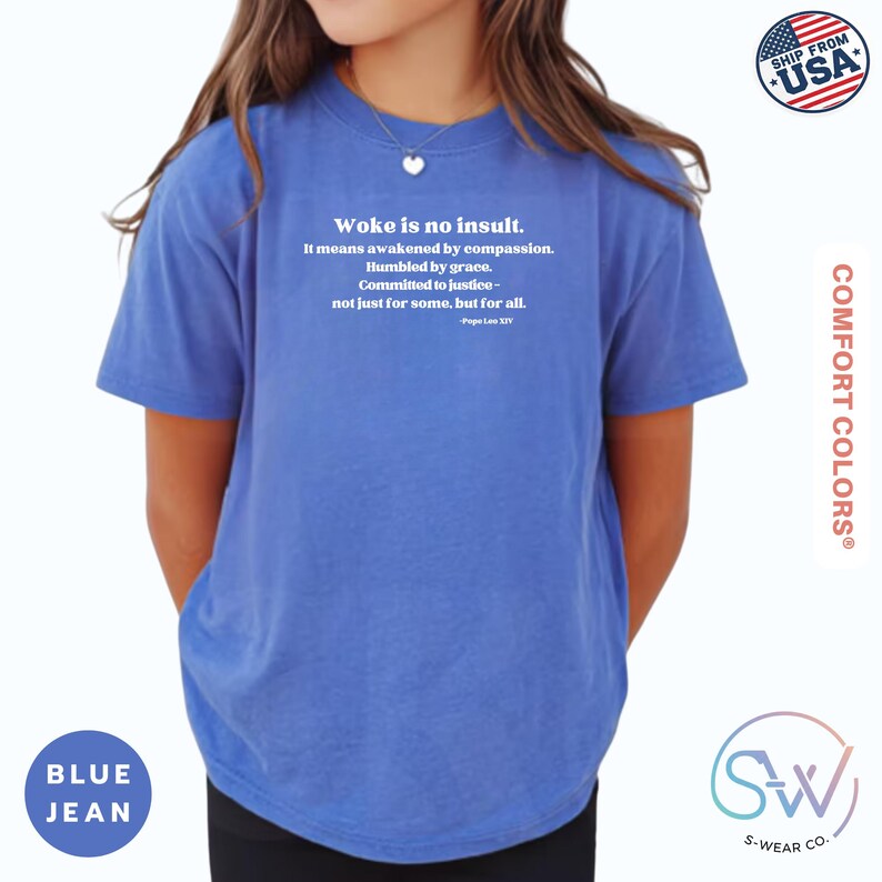 May include: Blue jean Comfort Colors t-shirt with the text "Woke is no insult." The text continues with a quote about compassion and justice. The shirt has a crew neck and short sleeves. The shirt is labeled "Ship from USA."