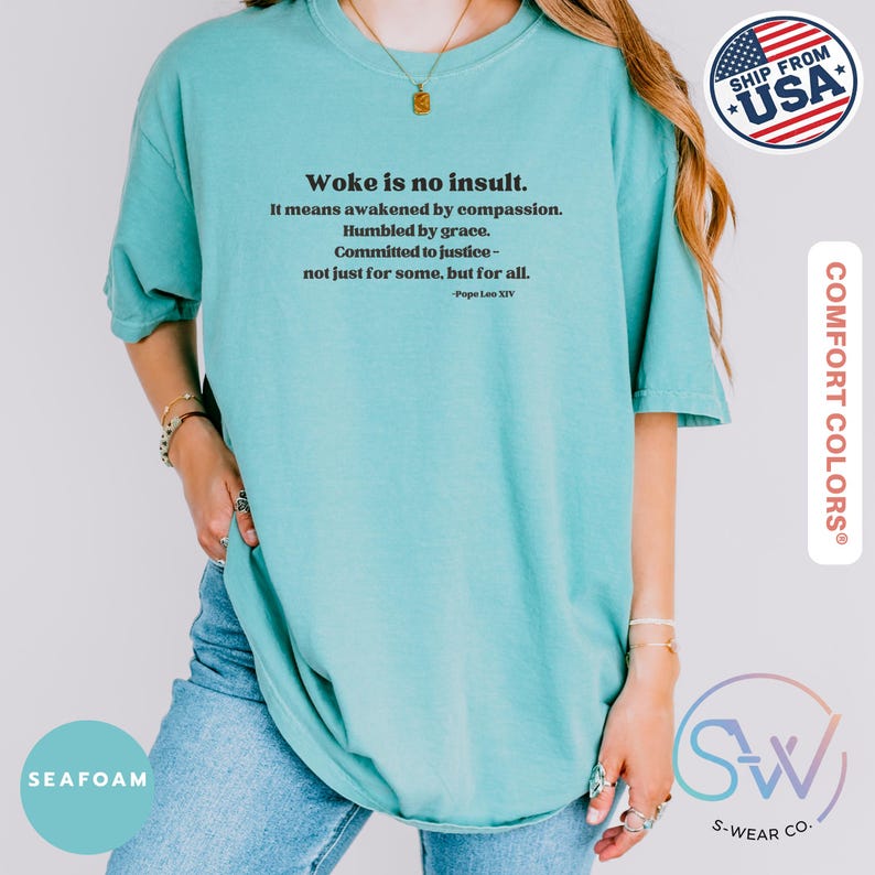 May include: Seafoam green t-shirt with the text "Woke is no insult." and a quote by Pope Leo XIV. The shirt is a Comfort Colors brand and features a relaxed fit. The image also includes a "Ship From USA" sticker.