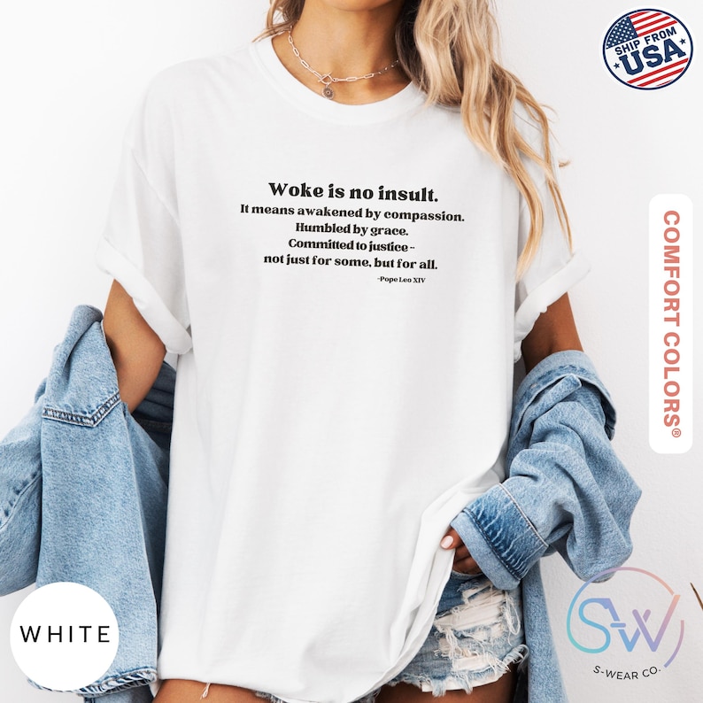 May include: White t-shirt with the text "Woke is no insult. It means awakened by compassion. Humbled by grace. Committed to justice - not just for some, but for all." The shirt is from Comfort Colors and has a "Ship from USA" graphic.