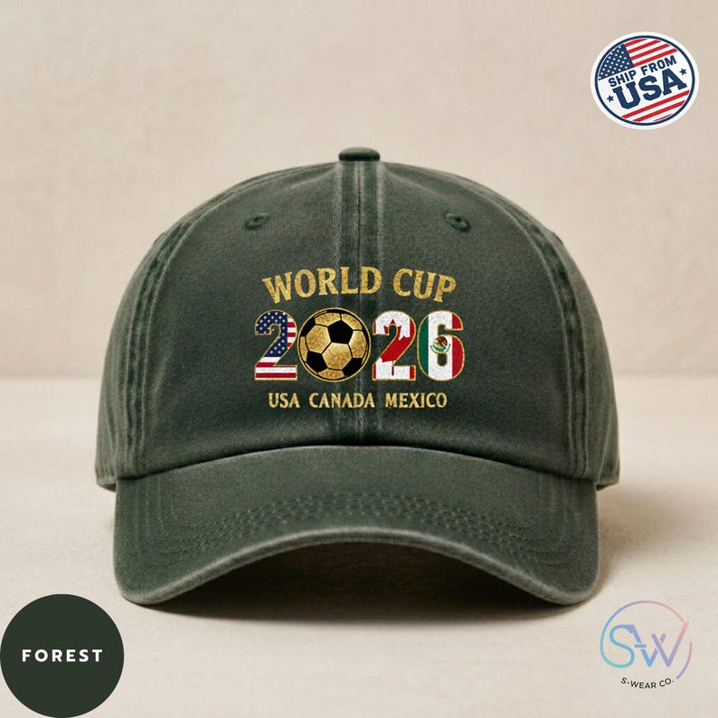 May include: A forest green baseball cap featuring the text "WORLD CUP 2026" in gold. The numbers 2026 are designed with a soccer ball and the flags of USA, Canada, and Mexico. The cap has a curved peak and a button on top.