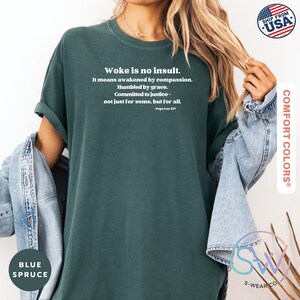 May include: Blue spruce Comfort Colors t-shirt with the text "Woke is no insult." in white. The text continues with a quote by Pope Leo XIV. The shirt has rolled-up sleeves and is paired with a denim jacket.