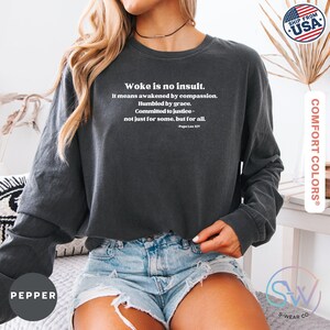 May include: Dark gray long-sleeve sweatshirt with the text "Woke is no insult." in white. The text includes a quote by Pope Leo XIV. The sweatshirt is made of Comfort Colors material.
