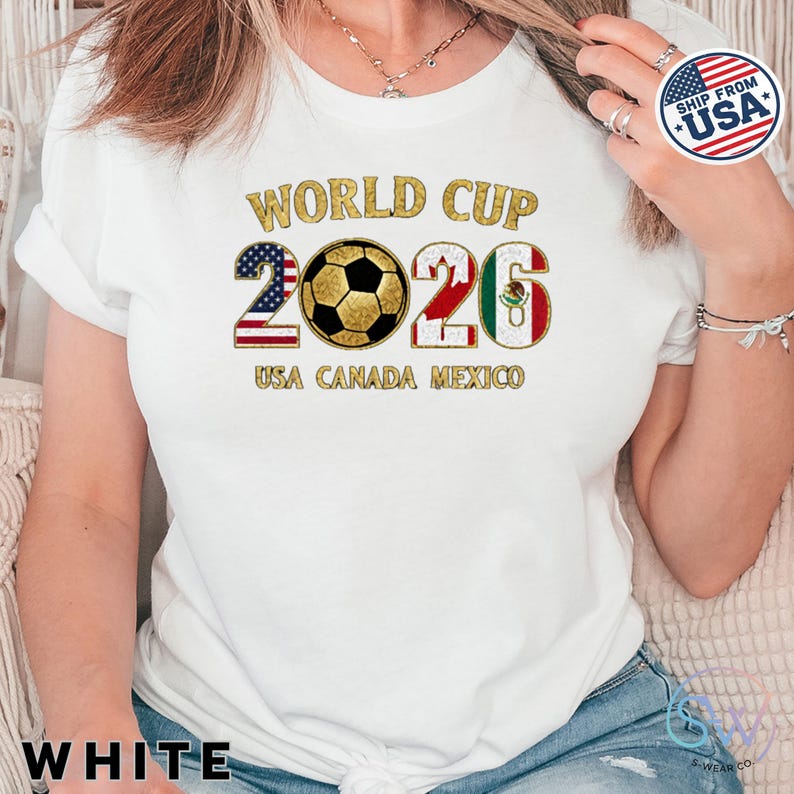 May include: White t-shirt with a gold-colored "World Cup 2026" graphic. The design includes a soccer ball and the flags of the USA, Canada, and Mexico. The text "USA CANADA MEXICO" is below the numbers.