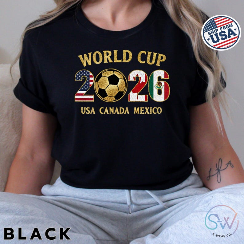 May include: Black t-shirt with gold text that reads "WORLD CUP 2026 USA CANADA MEXICO". The number 2026 is designed with the American and Mexican flags. A soccer ball is in the center. A "SHIP FROM USA" sticker is in the upper right corner.
