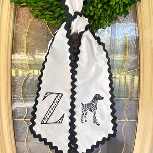 May include: White banner with a black scalloped edge, featuring a black and white dog illustration and the letter "Z". The banner is hanging on a glass door with a green wreath at the top.