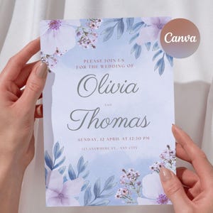 Può includere: Un invito di nozze con un design ad acquerello. L'invito presenta i nomi "Olivia" e "Thomas" in una scrittura elegante, circondati da accenti floreali e di foglie in tonalità viola e blu. Il testo "Please join us for the wedding of" è visibile.
