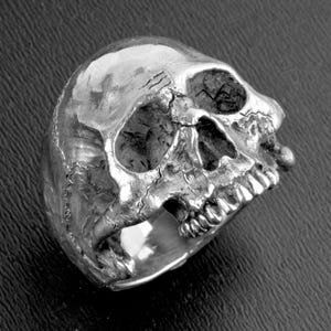 May include: A silver skull ring with detailed features, including teeth and eye sockets.