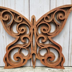 May include: A wooden butterfly wall decor with intricate cut-out designs. The butterfly is made of a light brown wood and has a natural finish.