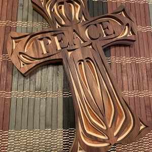 May include: A wooden cross with intricate carvings and the word "PEACE" in the center. The cross is made of dark wood with lighter wood accents.