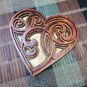 May include: A wooden heart-shaped wall decor with intricate carved patterns in shades of brown and light wood.