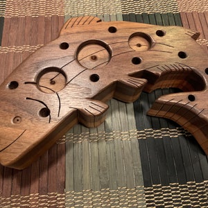May include: A wooden fish-shaped puzzle with multiple holes and a carved design. The fish is made of two different types of wood, creating a unique pattern.